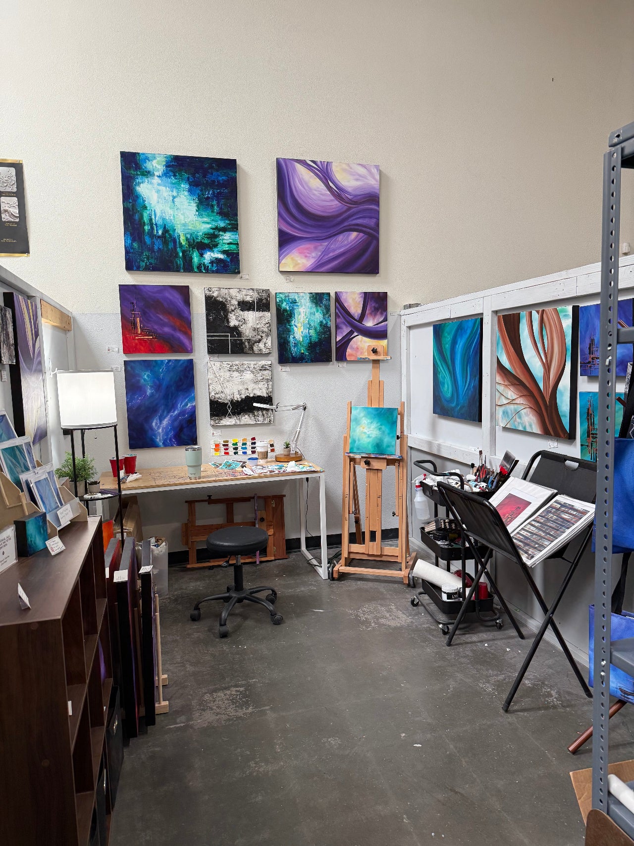Art studio with various paintings on the wall and a desk with art supplies.